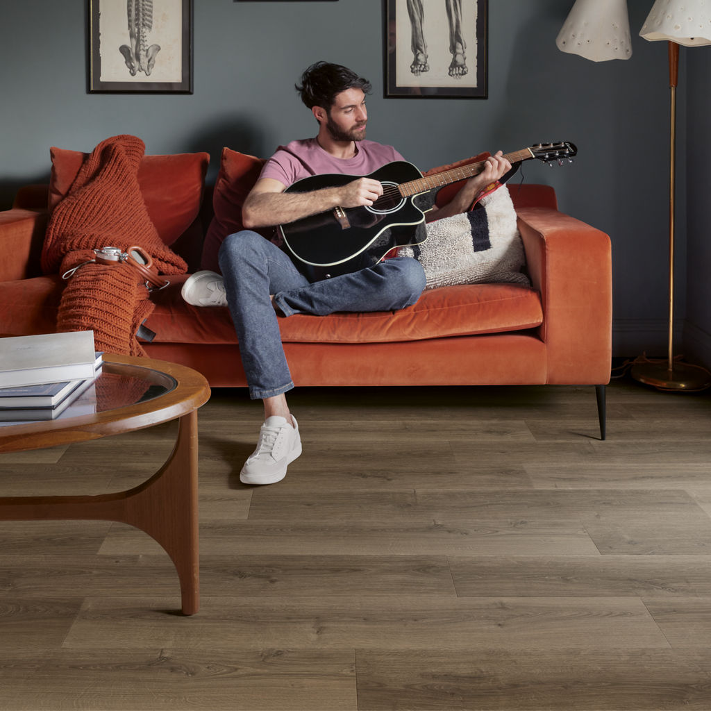 Salón con sofá naranja, hombre tocando la guitarra y suelo laminado Quick-Step Roble Marrón