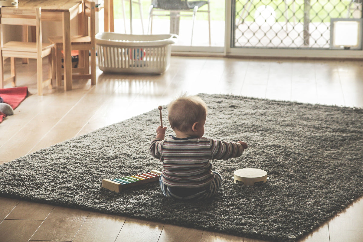 Bebé jugando sobre una alfombra en un salón con suelo de parquet laminado color miel