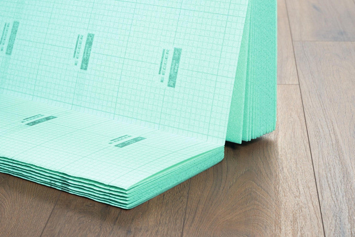 Base aislante EGGER Silenzio Easy de 2 mm: planchas verdes plegables con cuadrícula y logotipo EGGER, sobre suelo laminado