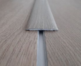 Perfil de expansión de PVC o aluminio adhesivo, color a juego con el suelo vinílico SPC Mundoparquet 4000 (2700 x 44 mm), colocado sobre la junta entre dos zonas de suelo