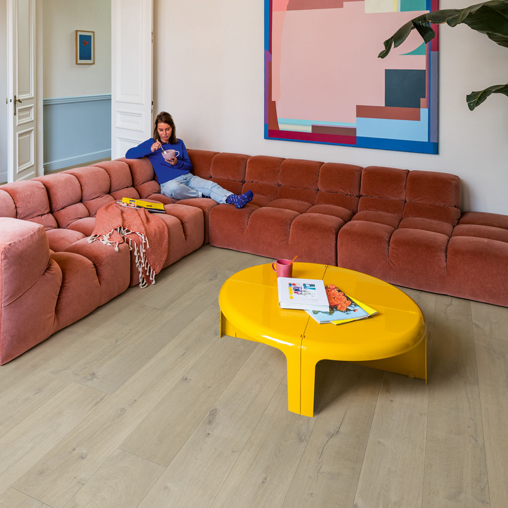 Salón colorido con sofá terracota, mesa amarilla y suelo laminado Quick-Step Roble Medio