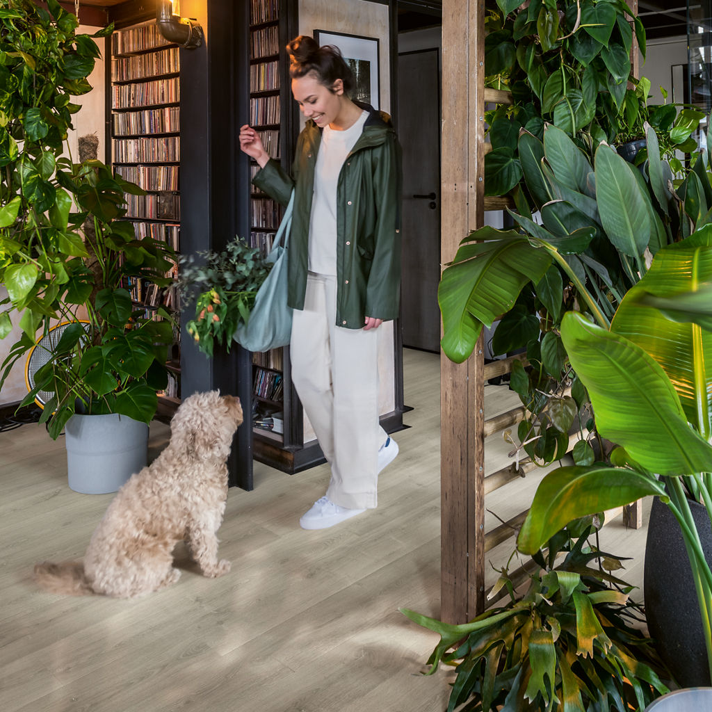 Entrada con suelo laminado gris Quick-Step y mujer con su perro entre plantas, estilo urbano