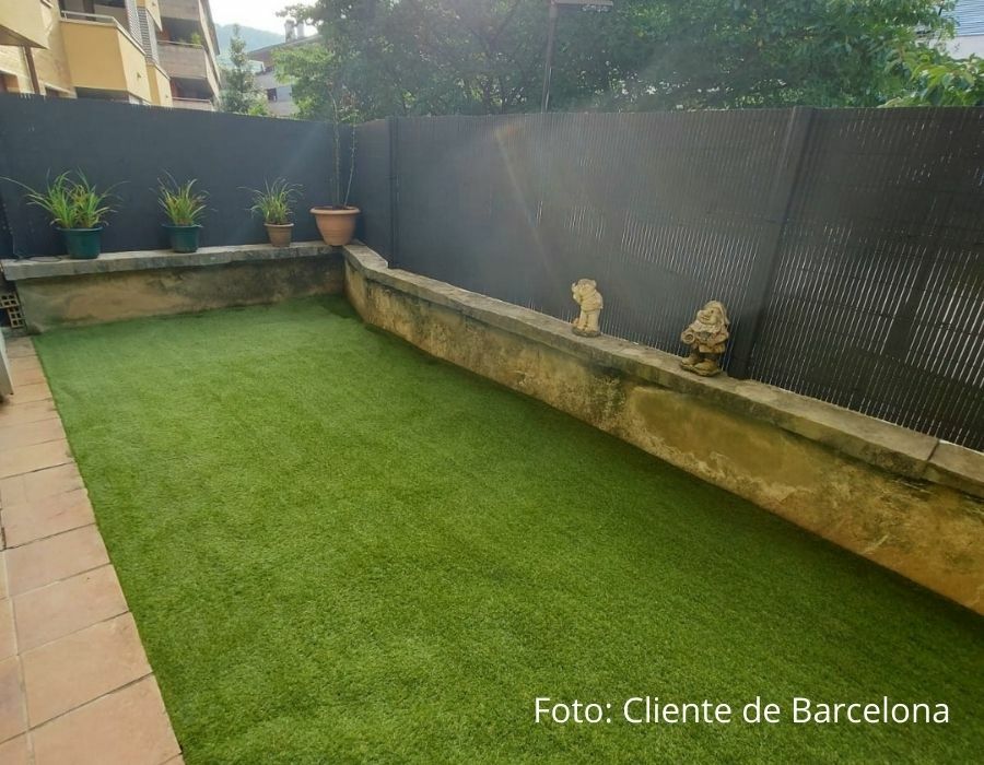 Terraza con césped artificial junto a un muro de piedra y plantas