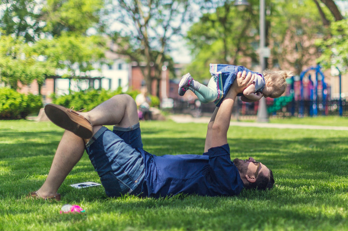 Padre jugando con su hija sobre el césped verde en un parque soleado