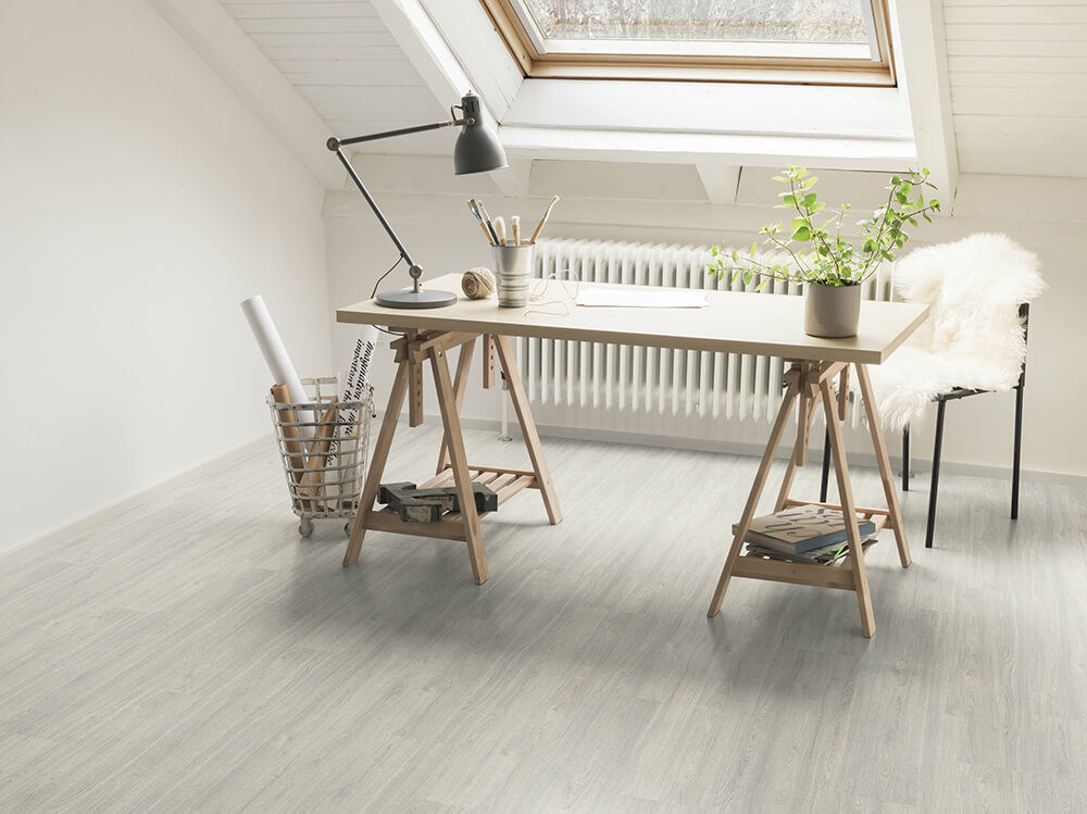 Buhardilla con escritorio de arquitecto y suelo laminado gris claro Egger bajo un tragaluz